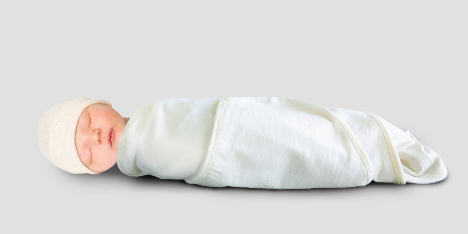 Baby sleeping in a merino cream swaddle wrap or swaddle blanket, also with a cream merino hat. The merino swaddle wrap is made in New Zealand. Similar to a swaddle blanket or swaddle wrap. Soft cream merino wool.